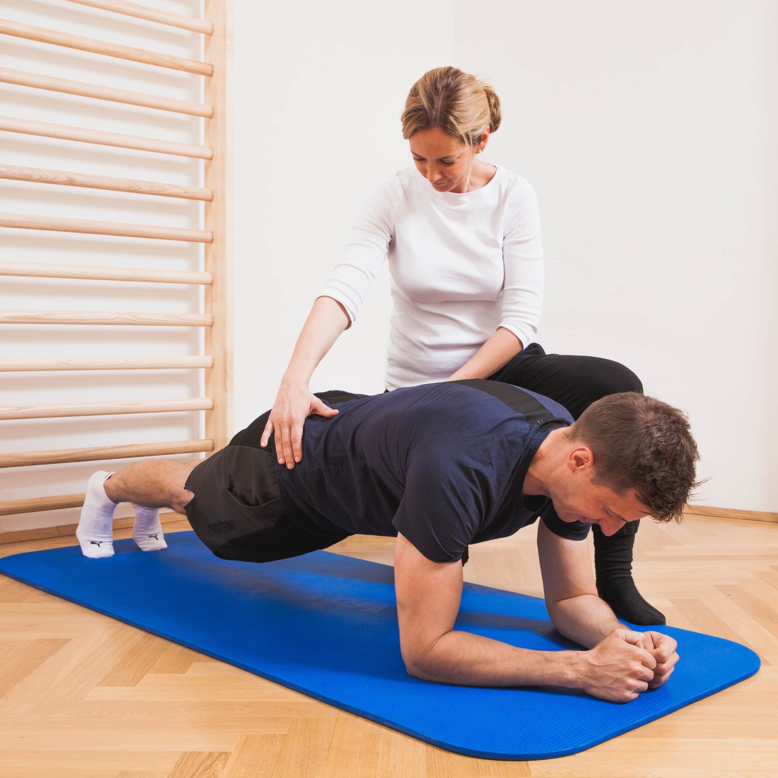 Physiotherapie Bednar. Arbeit von Physiotherapeutin Bednar an einem Patienten mit Rückenproblemen vor einer Sprossenwand